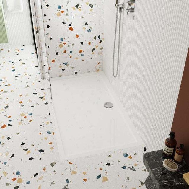 Nuie Rectangular Shower Tray Pearlstone in white installed in a modern bathroom with terrazzo tile flooring and a wall-mounted showerhead.